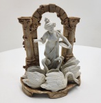 Peça em porcelana italiano, séc. XIX. Escultura representando jovem alimentando cisnes, modelada em biscuit branco sobre base com colunas e arco em tom ocre, evocando ruínas clássicas. O grupo apresenta três cisnes em alto-relevo ao redor da figura central, composição típica da produção decorativa italiana do período. Marca pintada a ouro na base. Trabalho harmonioso, de linhas suaves e acabamento delicado. Dimensões: 26 xx21x12 centímetros.