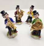 Conjunto raro de quatro figuras musicais em porcelana europeia, resultantes de manufatura Capodimonte com policromia aplicada nos ateliês de Dresden, representando jovens músicos em trajes clássicos, cada qual portando instrumento distinto. As peças apresentam modelagem típica napolitana, de volumes suaves e expressões vivas, enriquecidas pela paleta brilhante e detalhada característica de Dresden, com douramentos pontuais e forte apelo decorativo. Marcas em azul sob verniz, incluindo o N coroado de Capodimonte associado à inscrição Dresden, confirmando a dupla autoria. Dimensões: 14x7 centímetros cada. ( duas esculturas estão coladas)