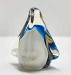 Peça decorativa em vidro artístico soprado, representando pinguim estilizado de linhas suaves e massa vítrea espessa, composta por corpo translúcido em tonalidade leitosa envolto por faixas trabalhadas em azul profundo e azul-claro, com sutis inclusões internas que evidenciam o processo manual de moldagem; figura de formato pleno e bem equilibrado, com volumes arredondados, asas insinuadas e cabeça levemente projetada, transmitindo equilíbrio formal e elegante simplicidade, típica da produção veneziana. Dimensões: 8x12x7 centímetros.
