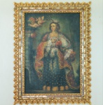 Virgem coroada por anjos, Escola Cuzquenha, século XVIII. Óleo sobre tela representando a Virgem em posição frontal, com vestes ricamente ornamentadas em motivos dourados e manto decorado com estrelas, características do vocabulário pictórico andino colonial. Dois anjos sobrevoam a cena, um deles coroando a figura com guirlanda florida, em composição típica da Escola de Cusco. A obra apresenta paleta grave em verdes, azuis e vermelhos profundos, com aplicação de douração decorativa. Moldura posterior em madeira dourada ao estilo barroco.Dimensões:1,43x1,07 com moldura.