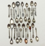 Lote composto por 25 colheres antigas em prata de lei, reunindo modelos decorativos e souvenirs de diversas origens. Inclui peças com cabos trabalhados, terminais figurativos variados e conchas lisas ou decoradas. Peso. 300 gramas.