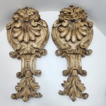 Par de talhas em madeira maciça no estilo barroco, grandes apliques de inspiração Rococó/Rocaille, apresentando concha central em destaque, volutas sinuosas, rocalhas e folhas de acanto em alto-relevo. Ornamentação movimentada e fluida, típica do vocabulário decorativo do século XVIII.Acabamento encerada e patinada, com desgaste natural do tempo, revelando camadas antigas. Verso com antigas marcas de fixação, indicando provável uso como ornamentos arquitetônicos ou aplicações de mobiliário.Dimensões: 69x33x12 centímetros.