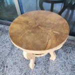 Mesa lateral redonda em madeira maciça, confeccionada a partir de seção sólida de tronco, evidenciando de forma natural os veios, anéis de crescimento e variações da madeira. Estrutura inferior com três pés curvos integrados a um prateleira circular, compondo desenho orgânico e escultural.A peça segue o conceito de mobiliário orgânico, valorizando a forma natural da madeira e sua textura, com acabamento acetinado que preserva a pátina e irregularidades originais. Dimensões: 0,63x0,62