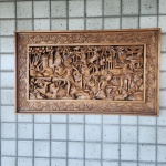 Grande painel retangular em madeira maciça, ricamente entalhado à mão em cena narrativa típica da arte balinesa. O conjunto apresenta figuras femininas em trajes tradicionais, animais (cervo, aves), elementos de vegetação tropical e arquitetura balinesa, incluindo templos e portais característicos.A composição é profundamente vazada e detalhada, com camadas sobrepostas de folhas, troncos e relevos florais, criando forte sensação de profundidade. A moldura, igualmente entalhada com motivos florais e rocalhas orgânicas. Dimensões:48x82centímetros.