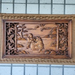 Painel retangular em madeira entalhada, representando duas crianças chinesas brincando ao redor de um grande tambor  motivo auspicioso associado à alegria, prosperidade e celebração. As figuras aparecem vestidas com trajes tradicionais, esculpidas em baixo e médio-relevo.O fundo apresenta paisagem estilizada com montanhas, nuvens auspiciosas, árvore sinuosa e arquitetura rural típica. Dimensões:30x53 centímetros.