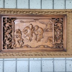 Painel retangular em madeira maciça, entalhado em alto-relevo, representando cena tradicional chinesa com duas crianças brincando, motivo associado à felicidade, abundância e boa fortuna. As figuras aparecem com trajes tradicionais e expressões delicadas, esculpidas com suavidade e bom detalhamento.As laterais do painel são compostas por entalhes vazados com arabescos, flores e elementos sinuosos, formando moldura ornamental típica da marcenaria sino-decorativa. O fundo exibe elementos paisagísticos estilizados, como montanhas, rochedos e árvores, seguindo a iconografia clássica do repertório oriental.