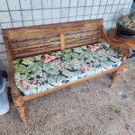 Banco em madeira maciça, de estrutura reta e braços suavemente curvos, ornados com entalhes manuais em volutas e motivos orgânicos. O encosto apresenta painéis vazados com elementos geométricos entrelaçados, típicos do mobiliário indo-balinês e do artesanato do Sudeste Asiático.As pernas frontais são torneadas, com frisos verticais e anéis decorativos. O assento acompanha almofadão estofado em tecido floral tropical (e, opcionalmente, almofadas lisas). Dimensões: 0,84x1,26x0,56.