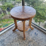 Mesa lateral redonda em madeira maciça, produzida artesanalmente em Bali. O tampo, de corte espesso, exibe veios naturais bem marcados, característicos de madeiras tropicais da região. A peça possui três pernas curvas, unidas por um prateleira circular inferior, reforçando a estrutura e oferecendo funcionalidade adicional. Dimensões: 62x49 centímetros.