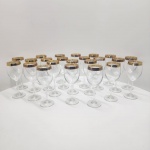 Conjunto composto por 23 taças em crista europeu, apresentando haste alongada, bojo clássico e acabamento superior adornado com borda dourada decorativa em padrão ornamental contínuo. As peças seguem modelo elegante. Taças de excelente transparência, brilho uniforme e som característico do cristal lapidado.Dimensões: 21x8 centímetros.  (Alguns apresenta do dourado).