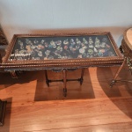 Elegante vitrine console estilo Luís XVI, finamente produzida em madeira entalhada, com acabamento em douração policromada e pátina envelhecida. O tampo apresenta visor em vidro plano, permitindo a exposição de pequenas coleções no interior, atualmente mostrando miniaturas (não incluídas, caso deseje especificar). A saia é ornamentada por festões decorativos em relevo, característicos do neoclassicismo francês.O móvel repousa sobre quatro pés torneados e estriados, unidos por travessas baixas, conferindo estabilidade e elegância. (Os itens que estão dentro não acompanha o lote) 0,77 x 1,12 x 0,47