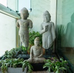 Conjunto composto por três esculturas balinesas talhadas em pedra vulcânica, material característico da produção artesanal de Bali, reconhecido pela textura porosa, tonalidade acinzentada e excelente resistência ao tempo. As peças apresentam equilíbrio entre simplicidade formal e suavidade expressiva, elementos marcantes da tradição escultórica da ilha.  Buda em pé  Mudra de ensinamento: figura esguia e serena, com o gesto vitarka mudra realizado pela mão direita. O tratamento do rosto, a suavidade do drapeado e o acabamento fosco da pedra vulcânica reforçam o caráter contemplativo da obra. Figura masculina balinesa  Torso ritual: representação de jovem figura cerimonial, com adornos florais em relevo e vestimenta tradicional. A ausência dos braços enfatiza o torso ornamental, em tipologia recorrente em esculturas decorativas balinesas.  Buda sentado  Posição de meditação: escultura do Buda em dhyna mudra, com pernas cruzadas e expressão introspectiva. A porosidade natural da pedra vulcânica. Dimensões: maior peça , menor peça 1,02x0,27x0,20