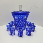 Elegante conjunto de ponche produzido em cristal overlay azul da Boêmia (Alemanha), caracterizado pelo contraste entre a camada externa azul cobalto e a lapidação profunda que revela o cristal incolor, criando desenhos geométricos e estrelas radiantes. Peça de grande presença decorativa e brilho excepcional.Acompanhado de 10 xícaras no mesmo padrão decorativo, com alças em cristal incolor, além de tampa facetada e concha também em cristal.A poncheira apresenta corpo alargado, rica lapidação em padrões losangulados, faixas cruzadas e motivos de estrela de oito pontas, típicos da produção boêmia da segunda metade do século XX. Dimensões 53x 40centímetros