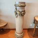 Imponente coluna decorativa confeccionada em terracota moldada, trabalhada em formato canelado de inspiração clássica. A peça apresenta acabamento patinado em tom marfim envelhecido, enfatizando o relevo suave das caneluras.Na porção superior, destaca-se uma guirlanda ornamental composta por flores, folhas e frutos em alto-relevo, com aplicação de douração envelhecida e nuances esverdeadas, criando contraste sofisticado e aparência de peça antiga.A base e a borda superior recebem friso decorativo com motivos vegetais, também realçados pela pátina dourada. Dimensões 1,30x0,41