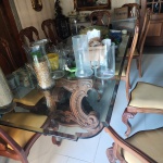 Conjunto composto por mesa de jantar em madeira maciça entalhada, com tampo retangular em vidro espesso, acompanhada por 10 cadeiras produzidas no mesmo padrão estético.A mesa apresenta base dupla em madeira esculpida, com volutas, folhas e arabescos decorativos, desenho característico de marcenaria artesanal clássica. O tampo em vidro transparente valoriza os entalhes da estrutura e confere leveza ao conjunto.As 10 cadeiras, igualmente em madeira entalhada, seguem o mesmo estilo da mesa, com espaldar recortado, ornamentos florais e arabescos contínuos. As pernas são curvas e os assentos estofados em tecido bege liso, criando composição uniforme e elegante. Dimensões: 0,77 x 2,74 x 0,74.