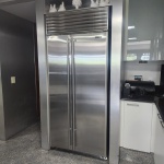 Refrigerador Sub-Zero de grande porte, modelo side-by-side, projetado para instalação embutida e acabamento arquitetônico. Estrutura integral em aço inox escovado, com portas duplas verticais, puxadores robustos e painel superior com grelha de ventilação característica da marca. Equipamento de padrão profissional, reconhecido por seu sistema de refrigeração dupla independente, controle preciso de umidade e vedação hermética  elementos que garantem desempenho superior e conservação prolongada dos alimentos. Peça de referência no segmento gourmet de luxo,