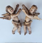 Par de putti em madeira entalhada, policromados e com douração em detalhes, representados em posição ascensional, com drapeados esvoaçantes e asas abertas trabalhadas em finas camadas. Expressões delicadas e volumetria bem modelada, com acabamento envelhecido que realça a textura da madeira e a pátina original. Peças de grande apelo decorativo, ideais para composição em parede ou em ambientes de linguagem clássica sacra. Excelente presença escultórica. 55x23x43 centímetros. ( cada).