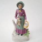 Figura de porcelana pintada à mão, representando camponesa idosa com cesto e ave. Trabalho europeu da segunda metade do século XX, com policromia fosca em tons suaves e base moldada. Peça decorativa de boa presença, típica das manufaturas populares do período. Dimensões: 30x14 x1p centímetros.