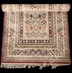 Elegante tapete decorativo de fabricação alemã, produzido à máquina, com desenho de inspiração caucasiana/armênia, composto por uma rica combinação de motivos geométricos, estrelas, cruzes estilizadas e padrões repetitivos distribuídos de forma simétrica ao longo do campo central. Com paleta luminosa em tons de creme, vinho, azul, verde e carmim, o tapete apresenta forte apelo decorativo e excelente definição de desenho, típica das tecelagens industriais alemãs, conhecidas pela precisão dos padrões e durabilidade dos fios. A estrutura é composta por fibras sintéticas e/ou mistura de fibras industriais (características desse tipo de produção), garantindo resistência, fácil manutenção e boa estabilidade dimensional. As franjas aplicadas reforçam o visual tradicional inspirado em tapetes orientais artesanais. Dimensões: 1,98x1,10