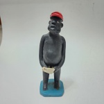 Escultura brasileira de Ernestina, cerâmica modelada e policromada.Figura masculina estilizada, de postura frontal, modelada em traços ingênuos característicos da produção de Ernestina. O personagem, de corpo alongado e volumes simplificados, apresenta expressão serena, usando boné vermelho e segurando pequeno recipiente nas mãos. A base em tom azul reforça o caráter decorativo da peça. Policromia original preservada, com assinatura ERNEST. incisa no verso.Exemplar representativo do artesanato figurativo popular brasileiro, destacando-se pela simplicidade formal, presença expressiva e linguagem escultórica singular da artista. Dimensões 20 x 7x7 centímetros