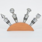 BEBIDAS, quatro (4) tampas para vedar garrafas de vinho, confeccionadas em metal, aros emborrachados,acompanha suporte expositor em madeira, medindo 19 x 10,5 x 2,5 cm, sinais de uso, vide foto.