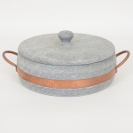 EQUIPAMENTO DE COZINHA, uma (1) panela com tampa, confeccionada em soapstone (pedra sabão), torneada,cinta e alça em metal cobreado, marca BRAS ART, medindo 24 cm diâmetro.