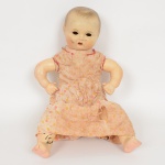 BRINQUEDO, uma (1) antiga boneca com cabeça e membros em papel marche, uma das pernas com, sinais detinta, corpo em tecido com enchimento, marcado em cavo na cabeça DISHA, boca aberta, olhos pendulares caídosdentro da cabeça, vestes em tecido, medindo 41 cm altura, sinais de uso, vide foto.