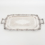 METAL PRATEADO, uma (1) bandeja retangular, fundo com ornamentação vegetalista em baixo relevo, bordareforçada e relevada em volutas e elementos vegetalistas, alças idem, medindo 37 x 23,5 cm mais as alças, sinais de uso,vide foto.