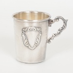METAL PRATEADO, um (1) copinho com alça, relevado em volutas, ligeiramente obcônico, ornado com escudo,puncionado SPAM, medindo 7 cm altura, sinais de uso, vide foto.