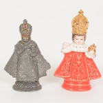 ARTE SACRA, duas (2) imaginárias representando Menino Jesus de Praga, sendo: 1 em pewter com apliques empolímero vermelho e facetados, possui perdas, medindo 7,5 cm altura; 1 em porcelana ou faiança, policromada e comdouração, medindo 8,5 cm altura, vide foto.