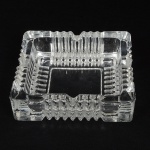 CRISTAL, um (1) cinzeiro quadrangular, incolor e translúcido, moldado em caneluras, medindo m15 x 15 x 4 cm,sinais de uso, vide foto.