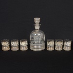 VIDRO, conjunto com sete (7) itens, incolores e translúcidos: 1 licoreira e 6 copinhos, ornamentação esmaltada emelementos vegetalistas, arremates com frisos a ouro já com sinais de desgastes, terço inferior em caneluras horizontais,tampa idem, defeito de fabricação próximo ao gargalo, medindo a maior peça 20 cm altura, sinais de uso, vide foto.