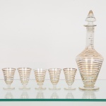 VIDRO, conjunto, anos 60, com seis (6) itens, incolores e translúcidos, sendo: 1 licoreira com tampa, ornada comfrisos dourados já com sinais de desgastes, base em bolacha, medindo 26 cm altura, acompanham 5 taças na mesmapadronização, medindo 6,5 cm altura, sinais de uso, vide foto.