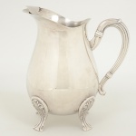 METAL PRATEADO, uma (1) jarra refresqueira bojuda, possui retentor de gelo, alça canelada, pés relevados emelementos vegetalistas, medindo 22 cm altura, sinais de uso, vide foto.Inicial