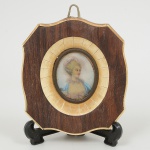 QUADRINHO, uma (1) miniatura representando busto de dama perfilado, policromada, moldura ovalconfeccionada em madeira e placas de marfinite, medindo 11,5 x 10,5 cm.