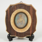 QUADRINHO, uma (1) miniatura representando dama com trajes antigos, policromada, moldura ovalconfeccionada em madeira e placas de marfinite, medindo 11,5 x 10,5 cm.