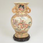 PORCELANA CHINESA, um (1) imponente vaso com ornamentação policromada representando paisagem comguerreiros a cavalo, montanhas e elementos vegetalistas, generosos arremates a ouro, marca de origem na base emlegenda e caracteres Made in China, além da palavra SATSUMA (possivelmente indicando o padrão utilizado, uma vezque é uma região do Japão), acompanha peanha em madeira torneada, ebanizada e com entalhes vazados, altura do vaso35,5 cm, peanha medindo 18 cm diâmetro e 3 cm altura, sinais de uso, vide foto.