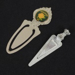 METAL PRATEADO, dois (2) marcadores de livro distintos: 1 souvenir de Vancouver, Canadá; 1 encimado porcachorro, medindo o maior 7 cm, ambos com sinais de uso, vide foto.