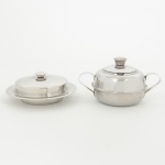 AÇO INOX, dois (2) itens: 1 manteigueira com tampa, marca MERIDIONAL, medindo 12,5 cm diâmetro; 1açucareiro com tampa, sem marca de manufatura aparente, medindo aproximadamente 10 cm diâmetro, ambos comsinais de uso, vide foto.