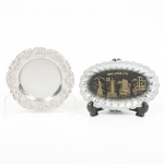 METAL PRATEADO, dois (2) itens distintos: 1 porta copos, confeccionado em aço inox, borda relevada em rosase volutas, medindo 10,5 cm diâmetro; 1 pequena travessa oval, borda canelada, ornamentação central com pontosturísticos de New York, confeccionada em folha de flandres, medindo 12,5 x 7,5 cm, ambos com sinais de uso, videfoto.