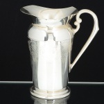 METAL PRATEADO, uma (1) jarra refresqueira, ornamentação em baixo relevo, base em degraus, possui retentorde gelo, manufatura EBERLE (Abramo Eberle 1880, Monte Magrè 1945, Caxias do Sul, veio com uma das primeiraslevas de imigrantes italianos para o Brasil em 1884 junto com seus pais Giuzeppe Eberle e Luigia Zanrosso, seu paiabriu uma pequena funilaria mas como tinha que trabalhar na lavoura quem cuidava era a mãe e o pequeno Abramoajudava na funilaria; em 1896 quando o pai resolveu vender a funilaria para concentrar os esforços da família na lavouraAbramo, com 16 anos de idade, se propôs a comprá-la do pai, em 1918 já com o nome Abramo Eberle & Cia iniciou afabricação de talheres e utensílios de mesa, morreu em 1945 com 65 anos de idade e os filhos deram continuidade aosnegócios até 1984 quando venderam para o Grupo Zivi), medindo 22 cm altura, sinais de uso, vide foto.