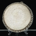 METAL PRATEADO, uma (1) salva que pertenceu ao militar A. M. Molina (serviu na Força Pública de São Paulono período da Revolução Constitucionalista), com diversas assinaturas, borda vazada em elementos vegetalistas, péscom terminações em garra, medindo 15,5 cm diâmetro, sinais de uso, vide foto.