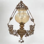 LUMINÁRIA, um (1) lustre de teto para um lume, estrutura em bronze com ornamentação relevada em elementosvegetalistas, pássaros, rostos e alegorias, cúpula em vidro na tonalidade amarela, furta cor, lapidada em sulcos e esferas,medindo aproximadamente 70 cm altura, encontra-se desmontado, parte elétrica ausente, vide foto.