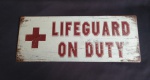 Placa decorativa em metal com emborrachados de efeitos envelhecidos e dizeres "LIFEGUARD ON DUTY' . Medida 18x46cm.