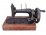 Antiga máquina de costurar para decoração com base em madeira e manivela também em madeira. Apresenta desgastes do tempo e manivela de madeira com rachado.