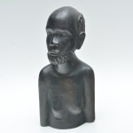 Busto masculino talhado em monobloco de madeira escura, com rosto definido, barba em relevo, cabelo texturizado por entalhes circulares e corpo simplificado. Apresenta leve fissura natural no topo. 27x13x12 cm.