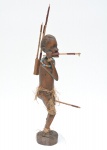 Arte africana - Escultura em madeira monobloco, representando figura masculina com colar de contas, fibras naturais no corpo e conjunto de lanças presas às costas. Traços faciais marcados e base integrada. 56x23x9 cm.