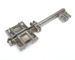 Chave em metal, de grandes dimensões conferindo caráter escultórico, sendo maciça, com empunhadura em forma de cruz vazada, de desenho geométrico e simétrico,  corpo apresenta haste longa e seção facetada. 21x8 cm.