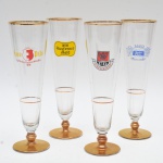 Conjunto de 4 taças longas para chope, em vidro transparente e esguias,  próprias para serviço de cervejas claras,  apresentam borda e filete interno em dourado, além de logotipos originais de cervejarias europeias aplicados em policromia, conferindo caráter publicitário e colecionável às peças, pés metálicos dourados. 23x7 cm