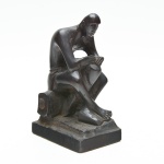 Escultura em madeira, entalhada em monobloco, destacando figura de postura introspectiva. Acabamento de pátina escura e base retangular. Marcas do tempo. 20x12x8,5 cm.