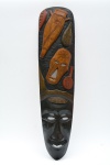 Máscara tribal de parede em madeira, entalhada manualmente, combina áreas em madeira clara e escura com tons avermelhado, com face estilizada de traços geométricos com destaque para grande peixe em relevo na parte superior. Verso escavado. 93x22 cm.